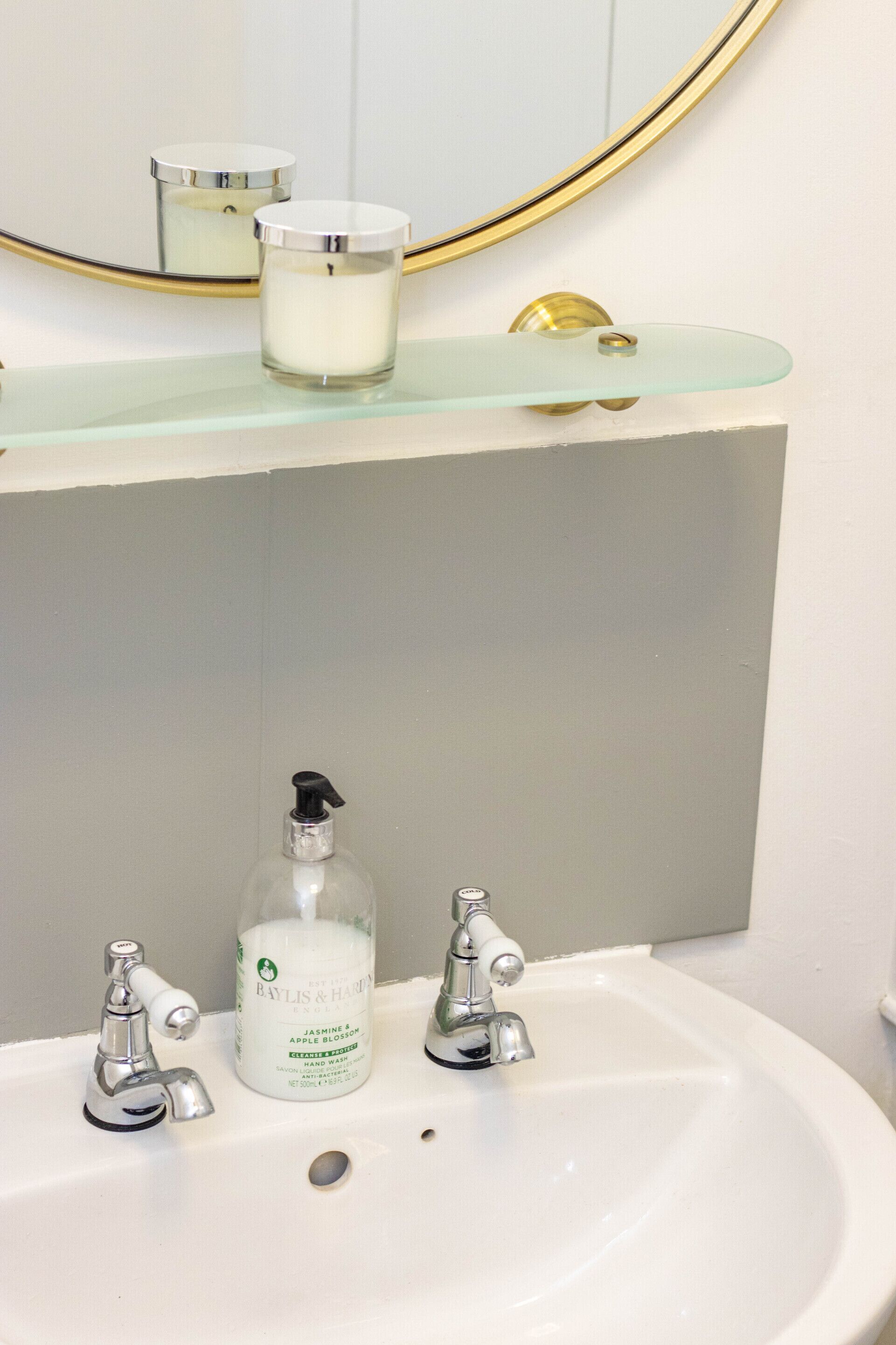 A bathroom with a white sink, two faucets, a glass soap dispenser, and a mirror with a gold frame.