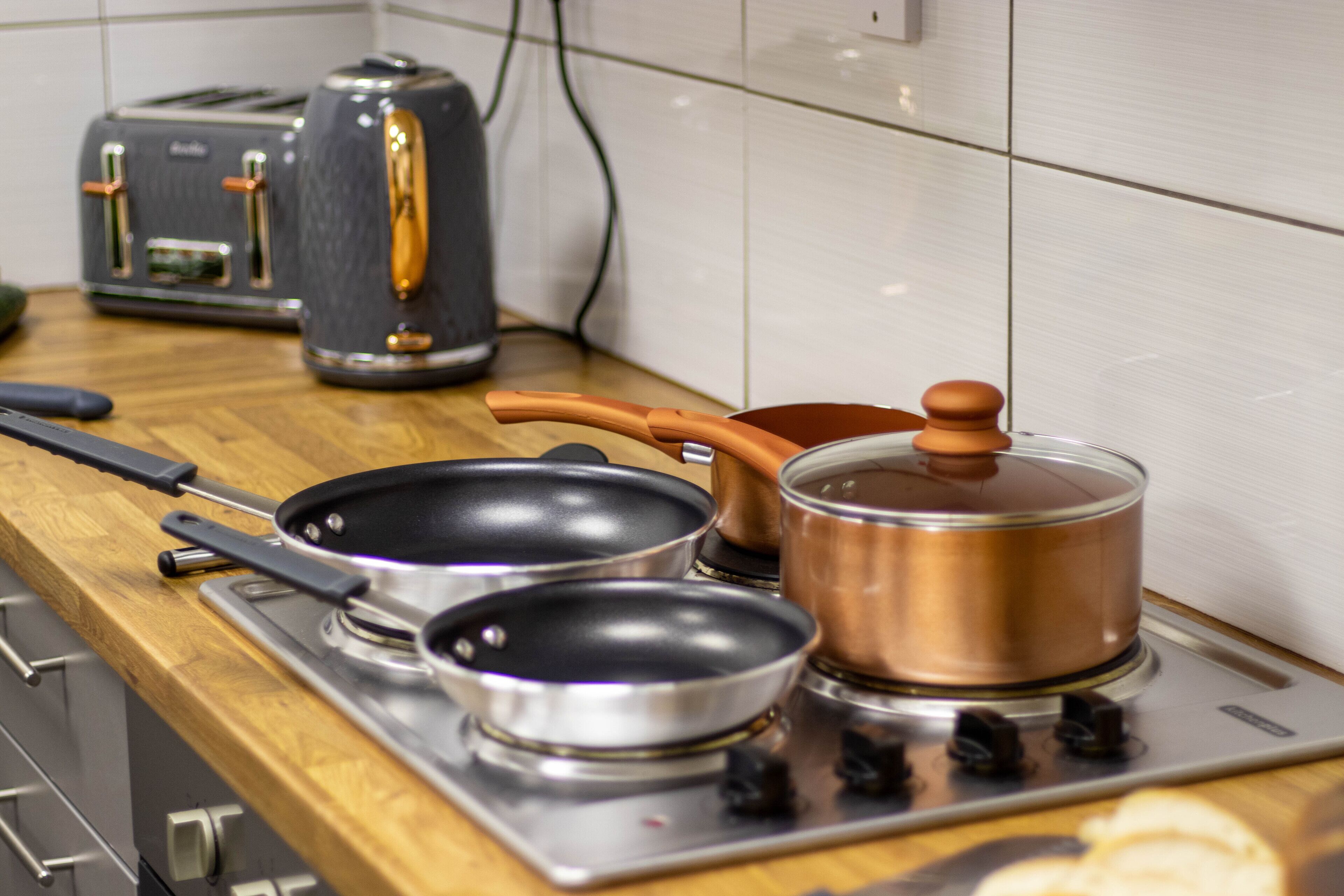 Een keuken met een fornuis, twee koekenpannen, een pan en een broodrooster.