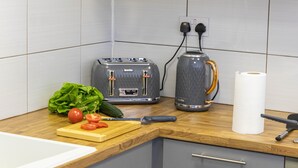 A kitchen with a toaster, kettle, and a cutting board with vegetables. - Cades Accommodation (Wolverhampton)