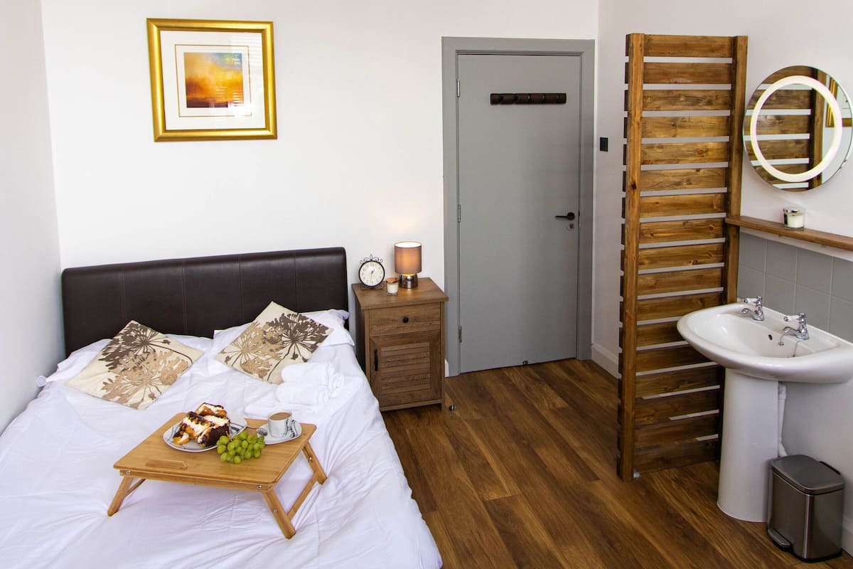 A bedroom with a bed, bedside table, lamp, and a wooden rack.