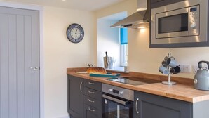 Een moderne keuken met donkere kasten, een houten aanrecht, een roestvrijstalen oven, een magnetron en een klok aan de muur.