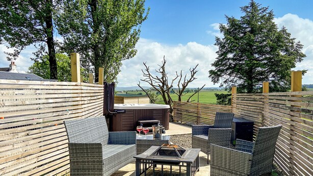 Een terras buiten met rieten meubels, een barbecue en uitzicht op het landschap.
