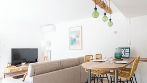 A modern living room with a sofa, TV, dining table, and hanging light fixtures. - Seaside villa sleeps 6, garden, air conditioning, garage (La Grande-Motte)