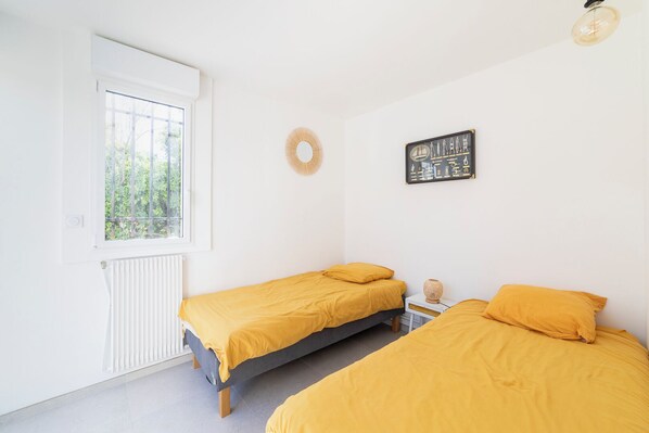 A bedroom with two beds, a window, a radiator, and a wall decoration.