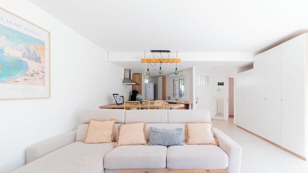 A modern living room with a white sofa, a wooden coffee table, and a kitchen in the background. - Seaside villa sleeps 6, garden, air conditioning, garage (La Grande-Motte)