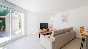 A modern living room with a sofa, a TV, and a dining area with chairs. - Seaside villa sleeps 6, garden, air conditioning, garage (La Grande-Motte)