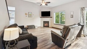 A modern living room with a fireplace, leather sofas, a flat-screen TV, and a ceiling fan. - Spacious 4 BR Home Convenient Location (Tiffin)
