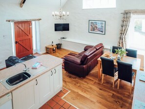 Eine moderne Küche mit integriertem Spülbecken, einem Essbereich mit Holztisch und -stühlen, einem Ledersofa und einem an der Wand befestigten Fernseher.