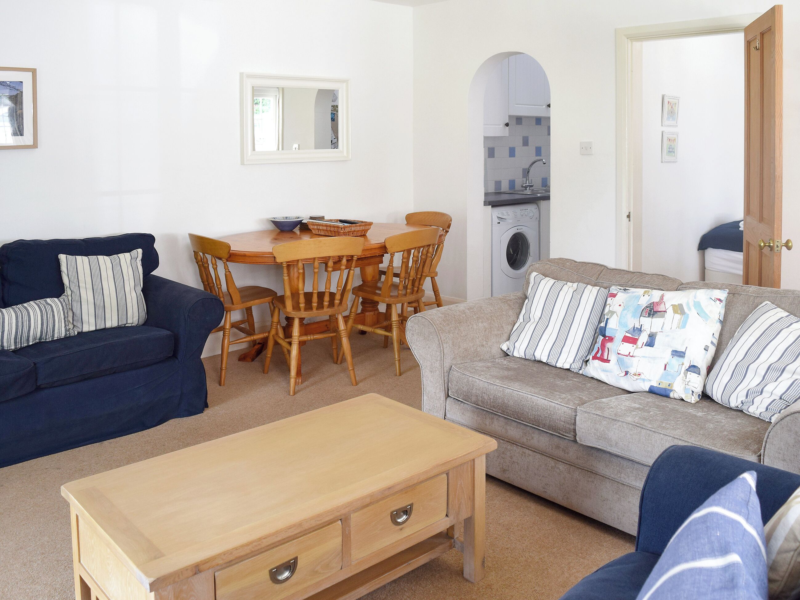 A living room with a blue sofa, a grey sofa, a wooden coffee table, and a dining table with chairs.