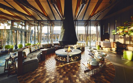 A spacious lounge area with a central fire feature, comfortable seating, and large windows offering views of the outdoors.