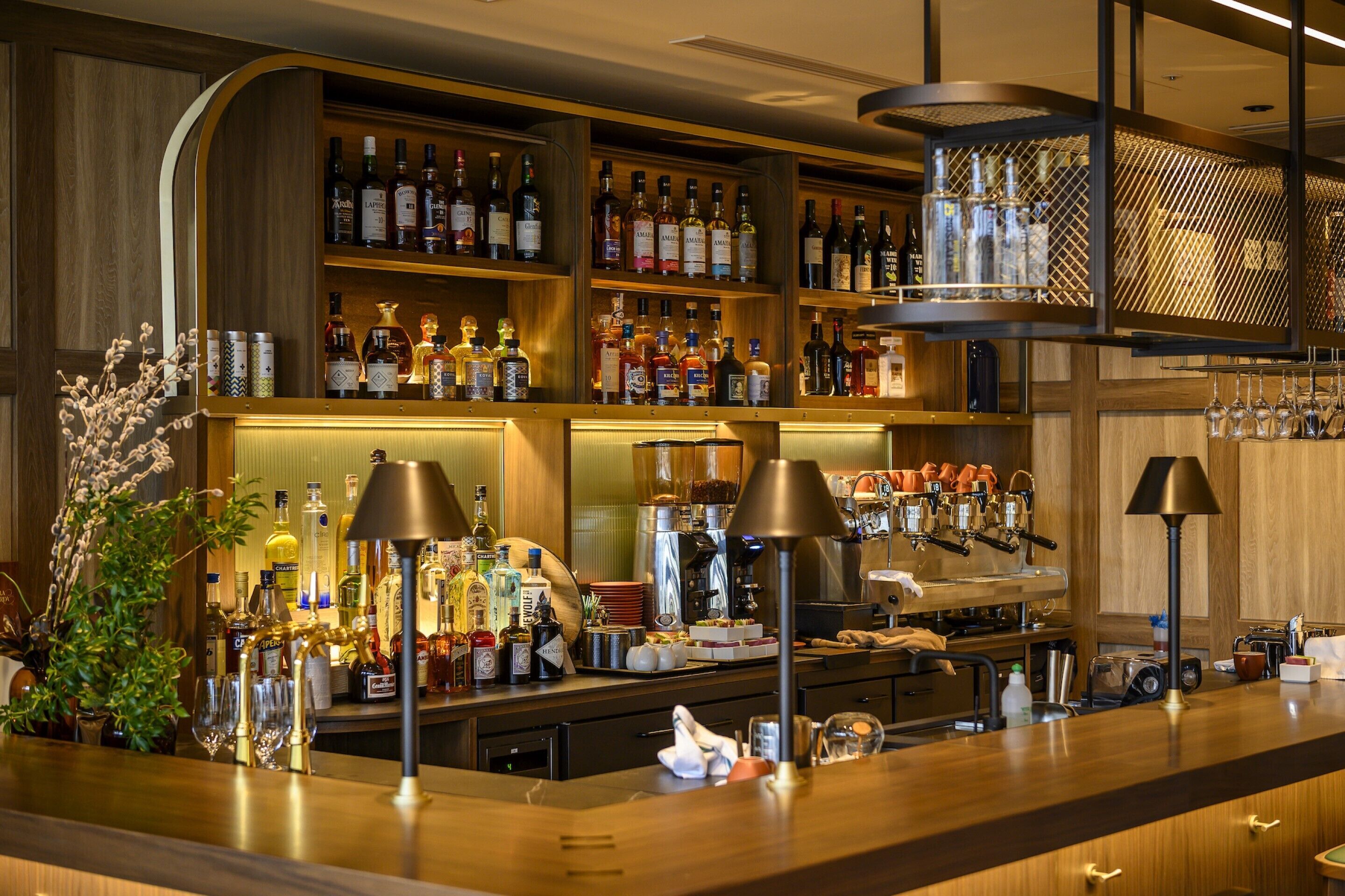 Un espace bar avec des étagères remplies de bouteilles d’alcool, une machine à café et des ustensiles de bar.