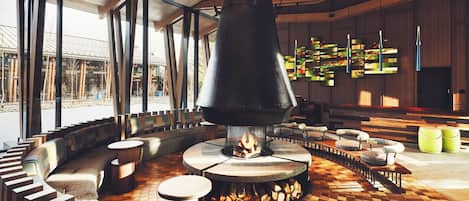 Un interior moderno con una chimenea central, zonas de estar y grandes ventanales.