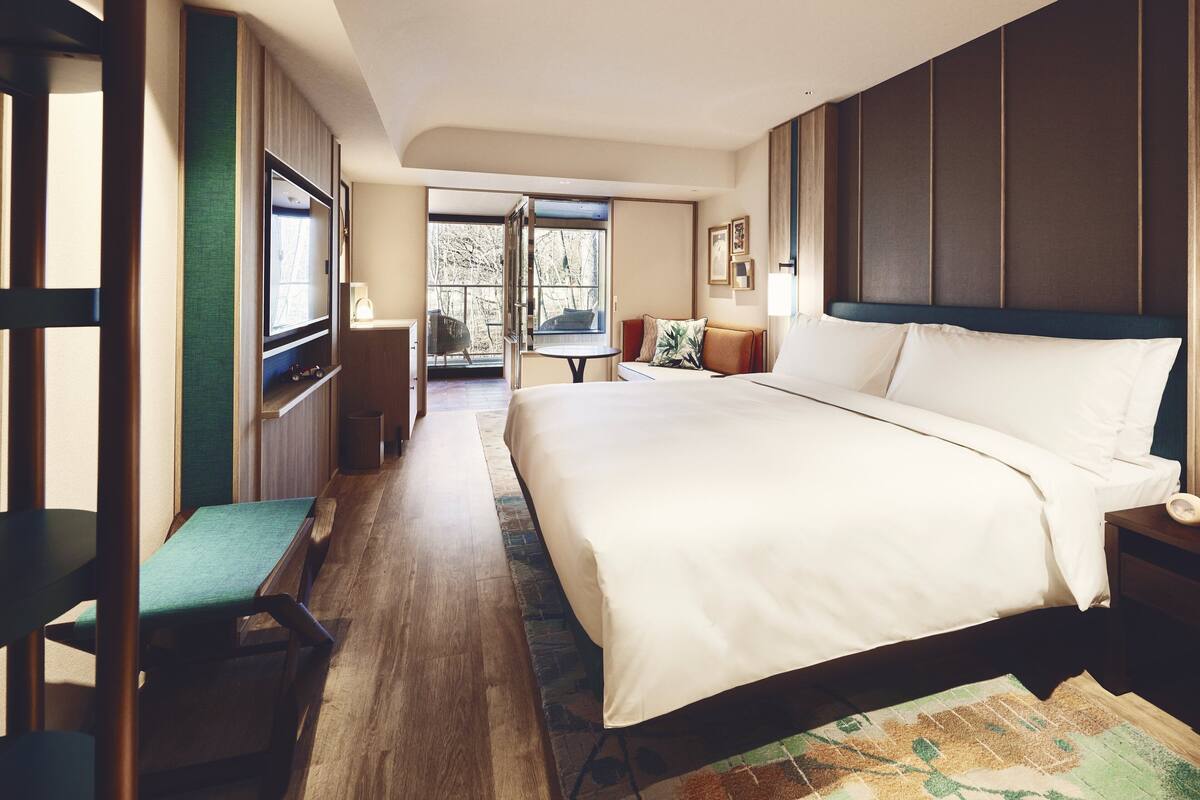 A hotel room with a large bed, a seating area with a table, and a view of the outdoors through a glass door.