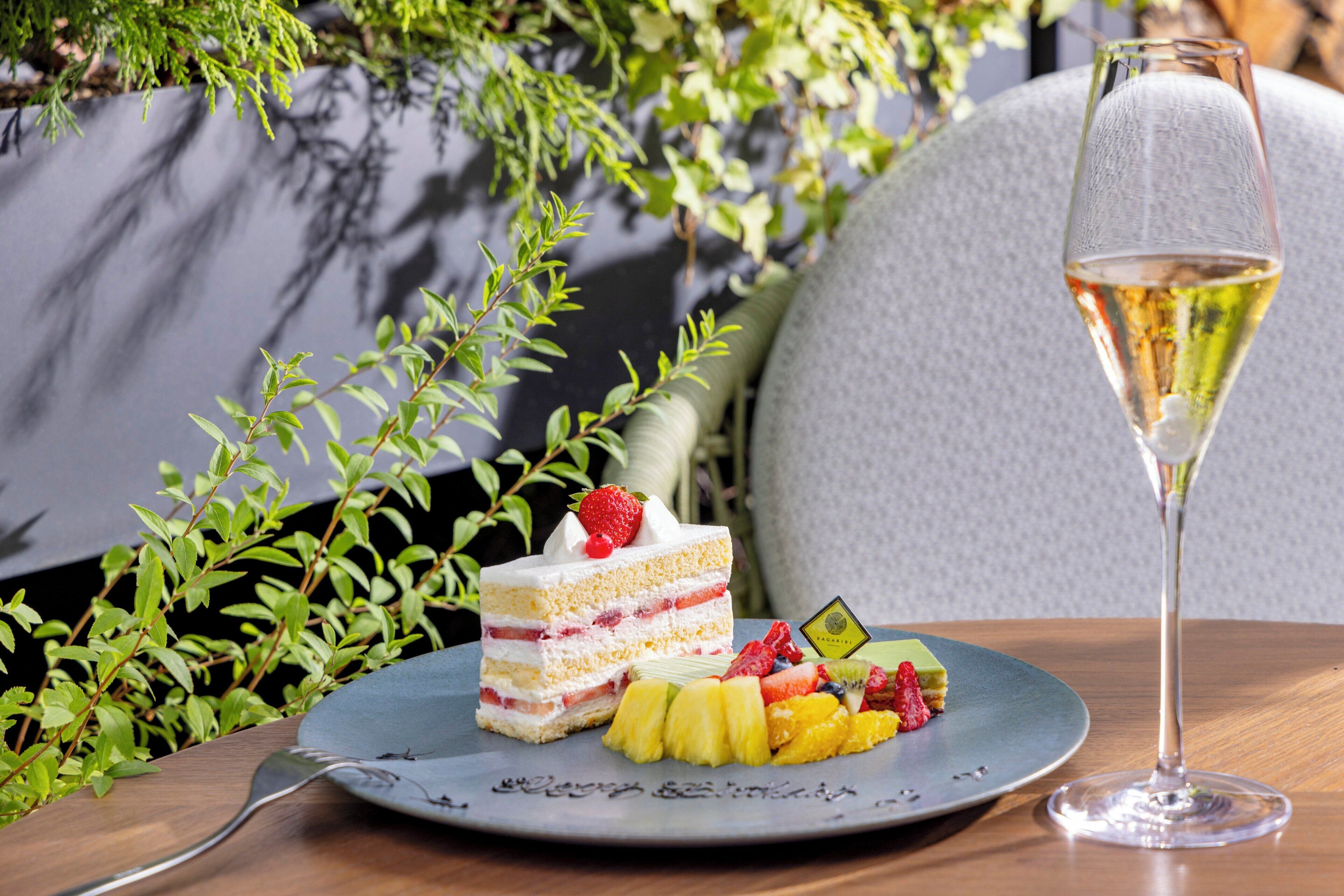 Un plato con un pastel en capas, fruta y una copa de vino blanco sobre una mesa.