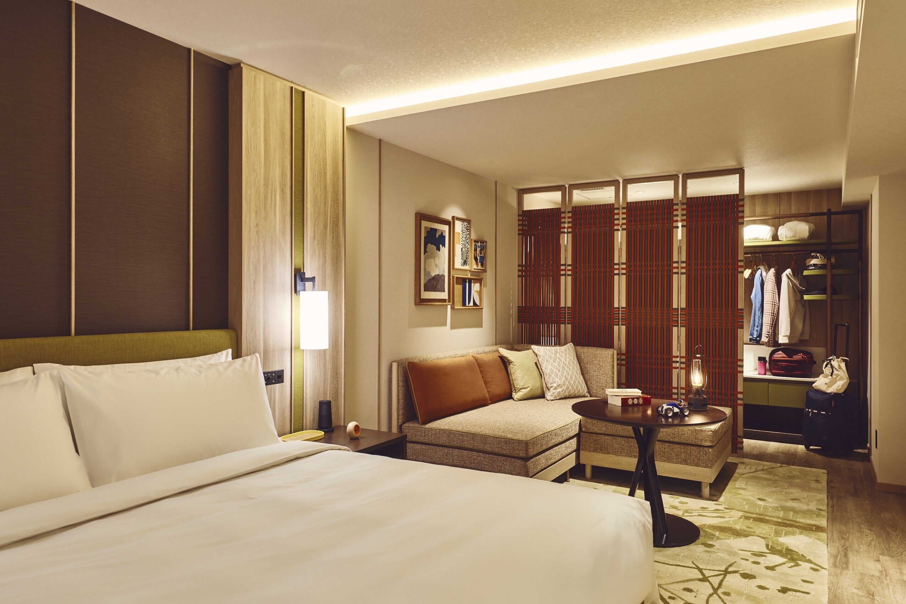A hotel room with a bed, a sofa, a small table, a closet, and a decorative lamp.