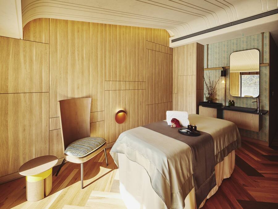 Ein modernes Schlafzimmer mit einer Wandpaneelaus Holz, einem Bett mit beigefarbener Bettdecke, einem Nachttisch, einem Sessel und einem Spiegel.