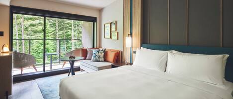 A hotel room with a large bed, a seating area with a table, and a view of greenery through the window.
