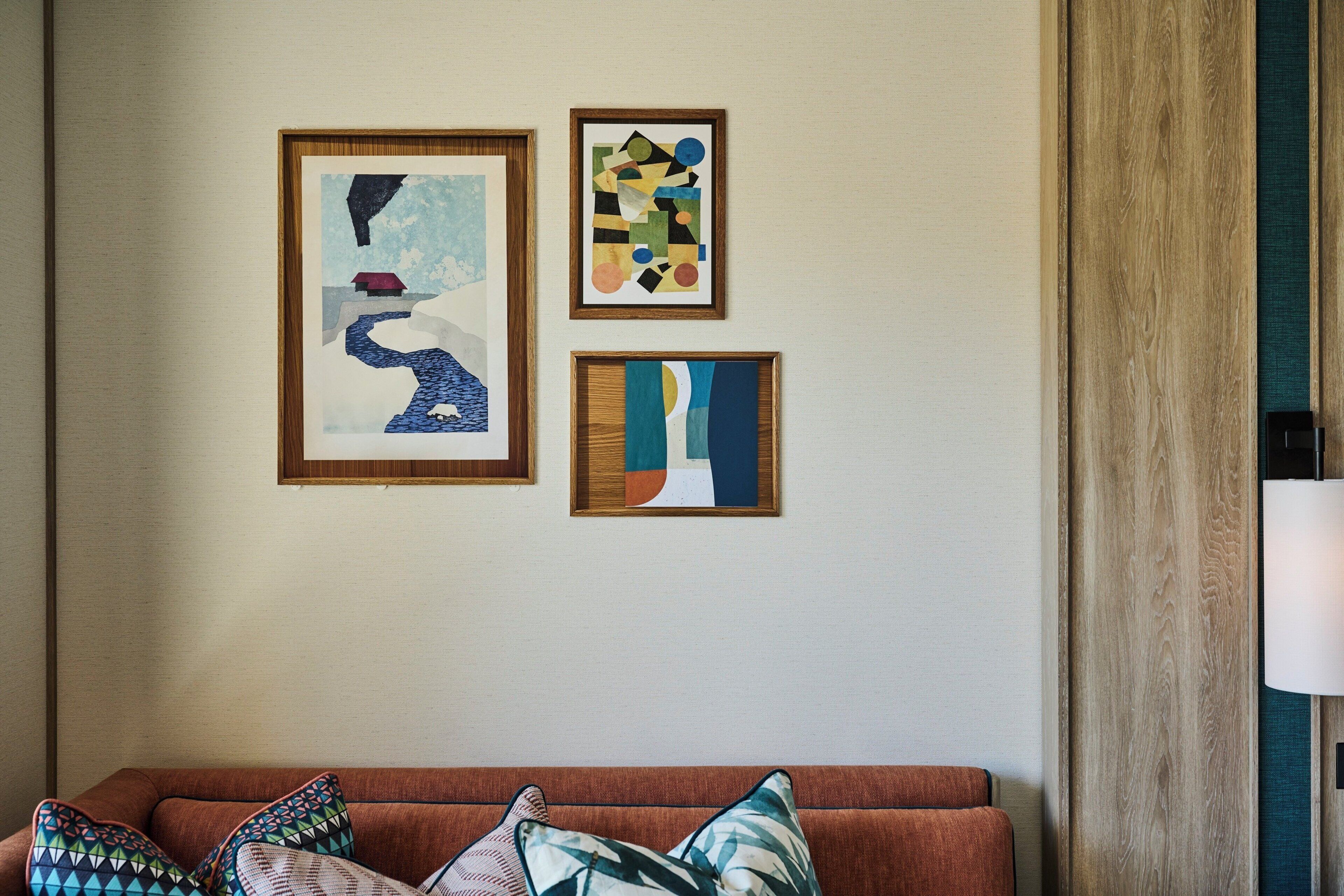 A room with a brown sofa and three framed artworks on the wall.