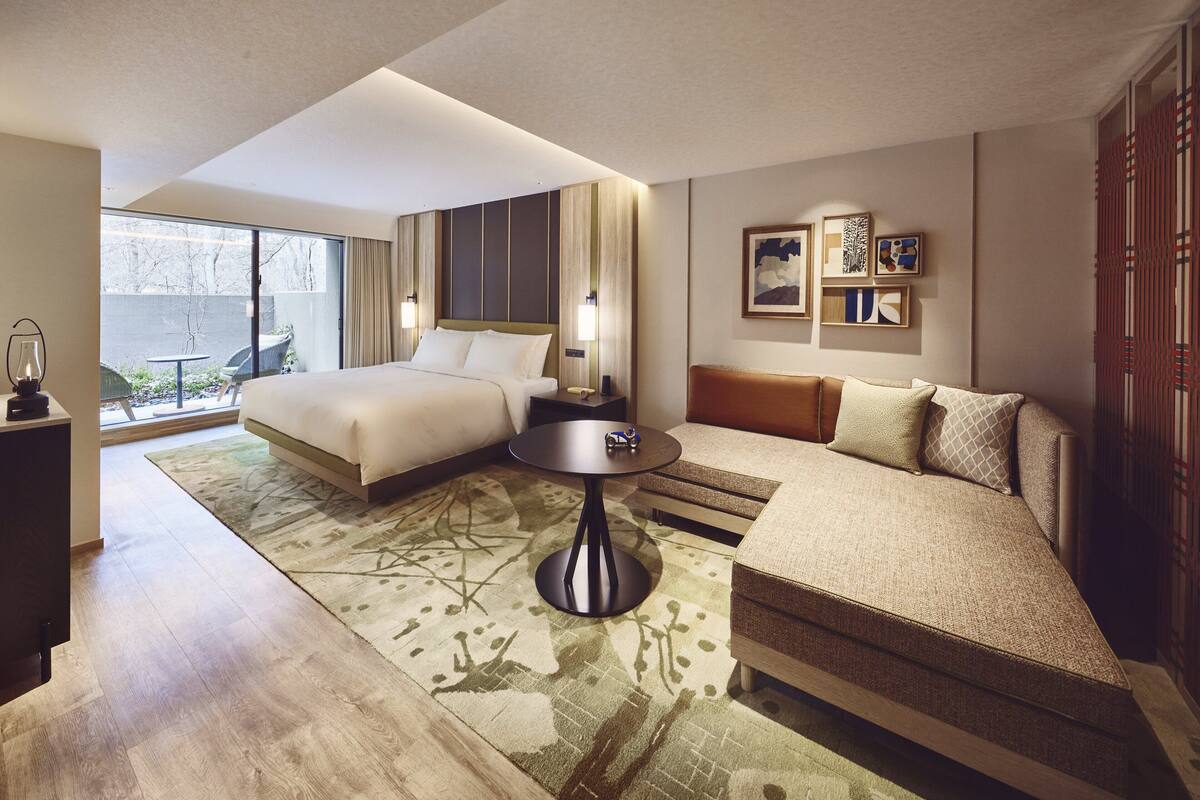 A hotel room with a bed, a sofa, a small table, and a view of the outdoors.
