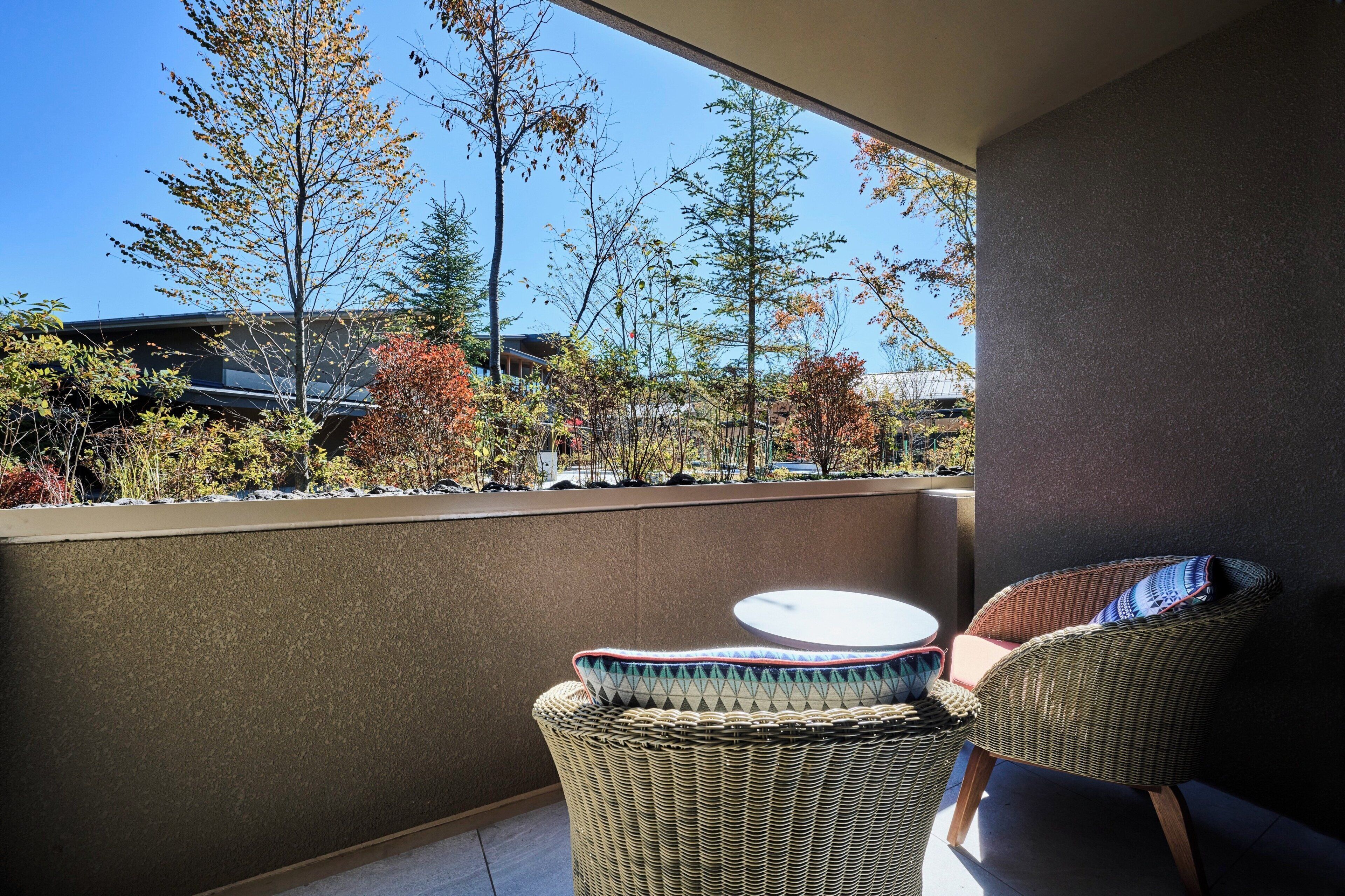 A balcony with wicker furniture, a small round table, and a view of trees and buildings.