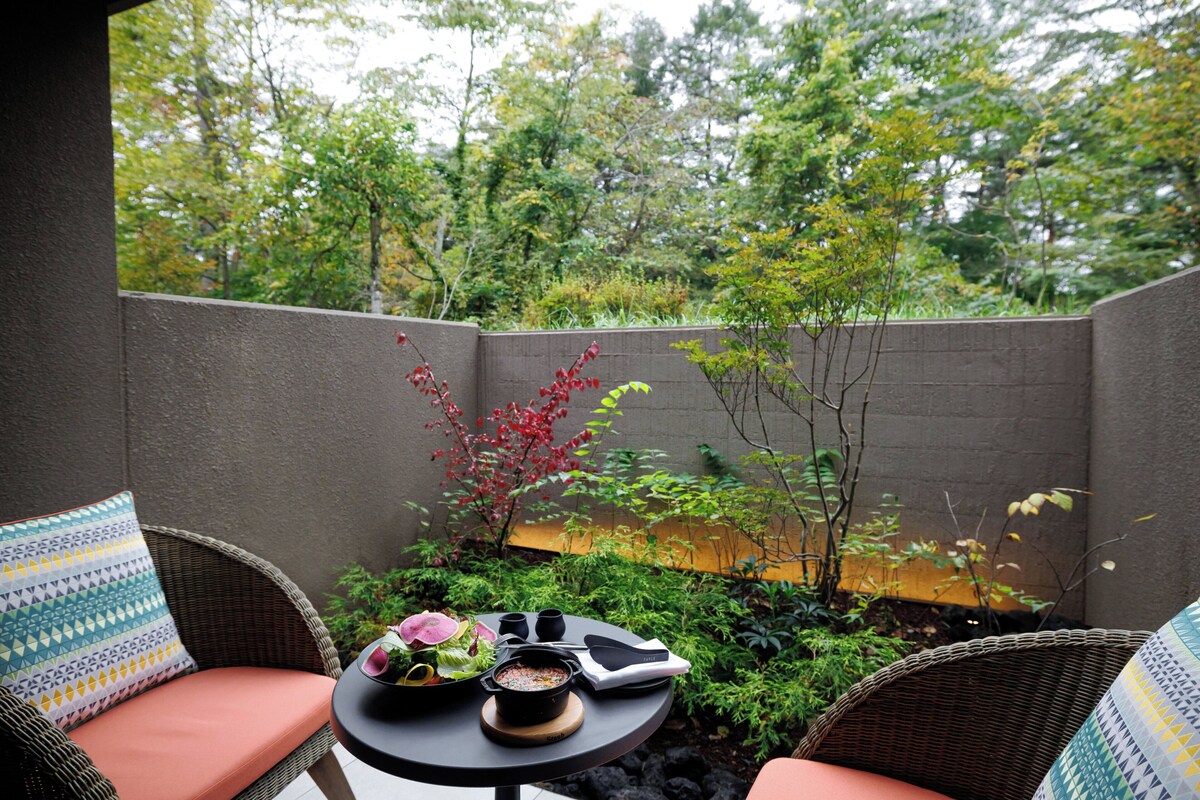 A patio with wicker furniture, a small round table, and a view of a garden with trees and plants.