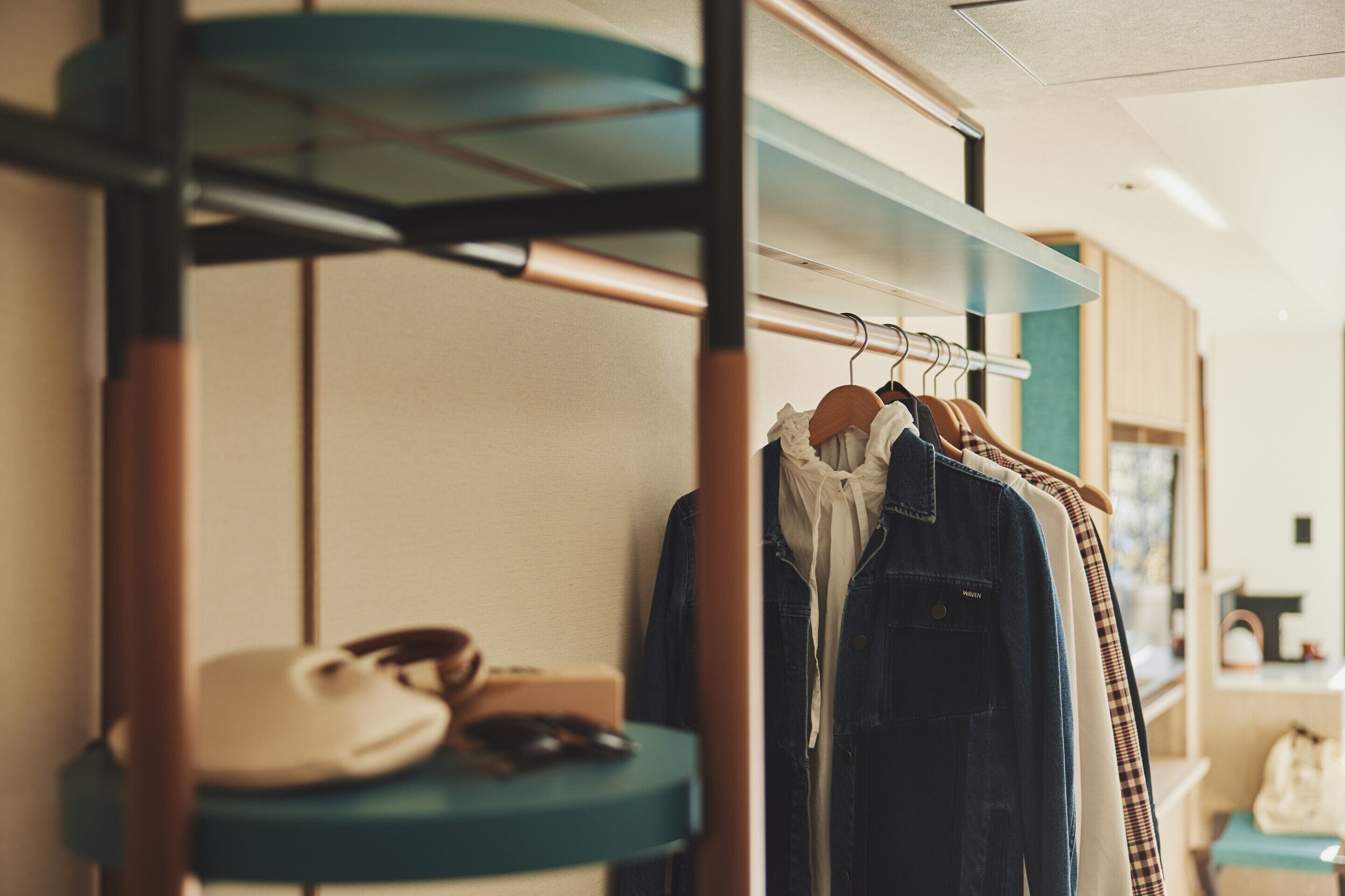 A clothing rack with various garments, a pair of shoes, and a small table with a cup and a bag.