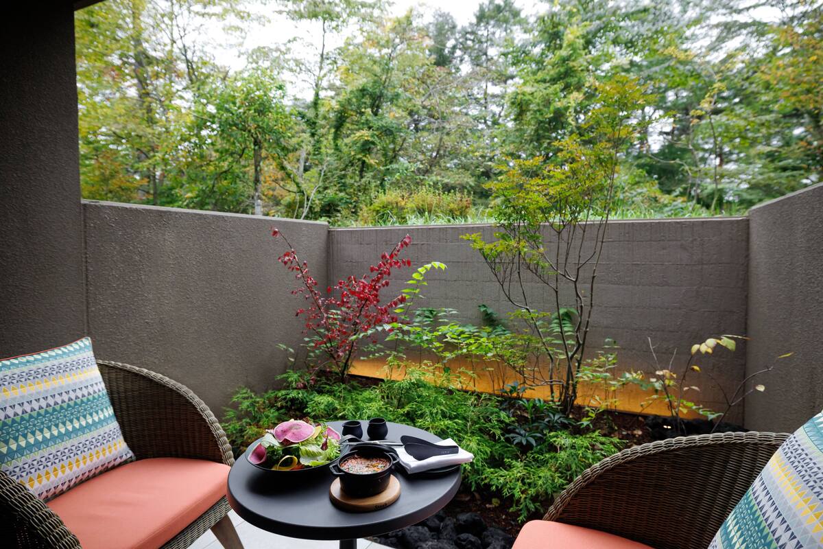 A patio with wicker furniture, a small round table, and a view of a garden with trees and plants.