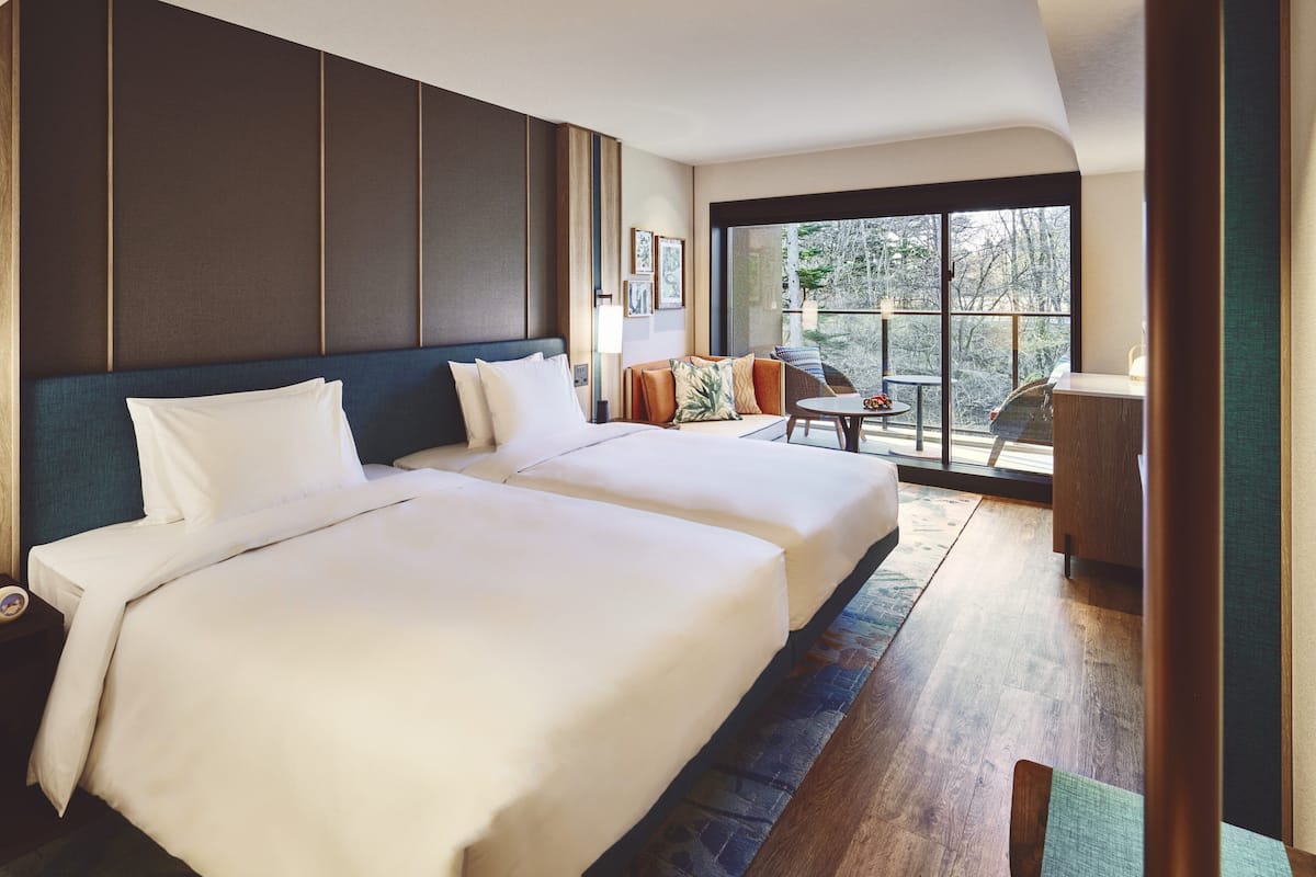 A hotel room with two beds, a small table, and a view of the outdoors.