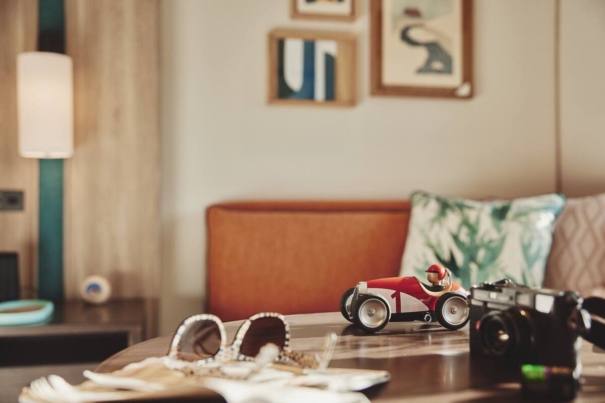 A room with a wooden headboard, a small table with a toy car and a camera, and a lamp on a side table.