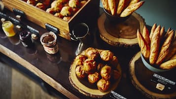 Une présentation de viennoiseries et de pains sur des planches en bois, avec des pots de confitures et une tasse de café.