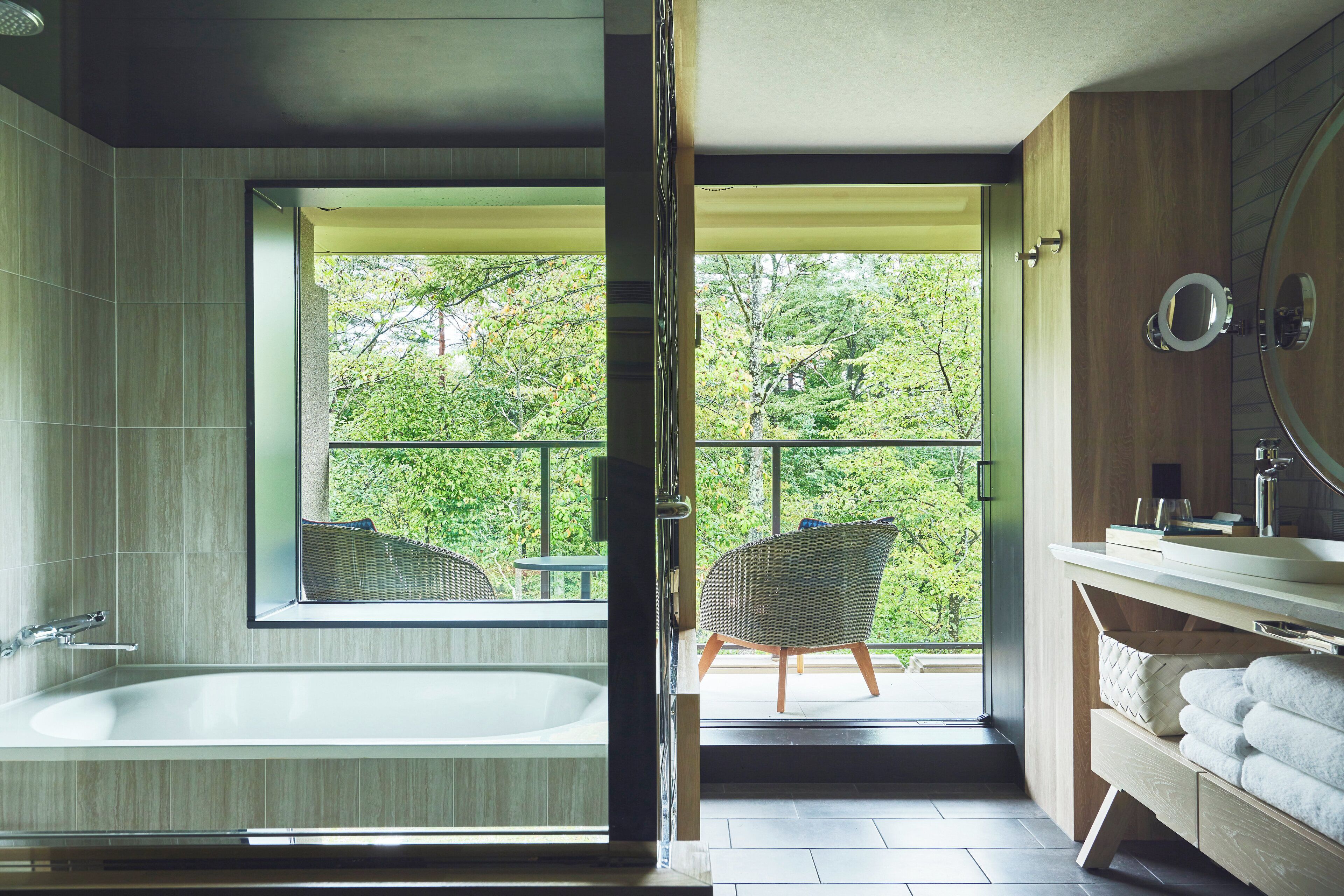 Une salle de bain moderne avec une baignoire, une grande fenêtre et une vue sur la verdure.