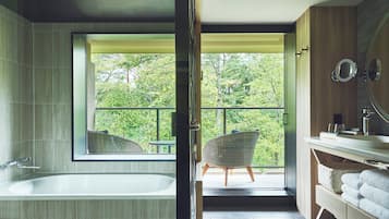 Un baño moderno con bañera, un ventanal grande y vistas a zonas verdes.