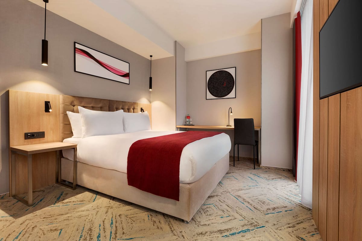 Een moderne hotelkamer met een groot bed, nachtkastje en een bureau met stoel.
