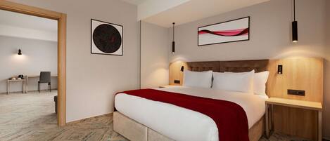 Una habitación de hotel moderna con una cama grande, dos mesitas de noche, un cabecero y suelo cubierto de alfombra.