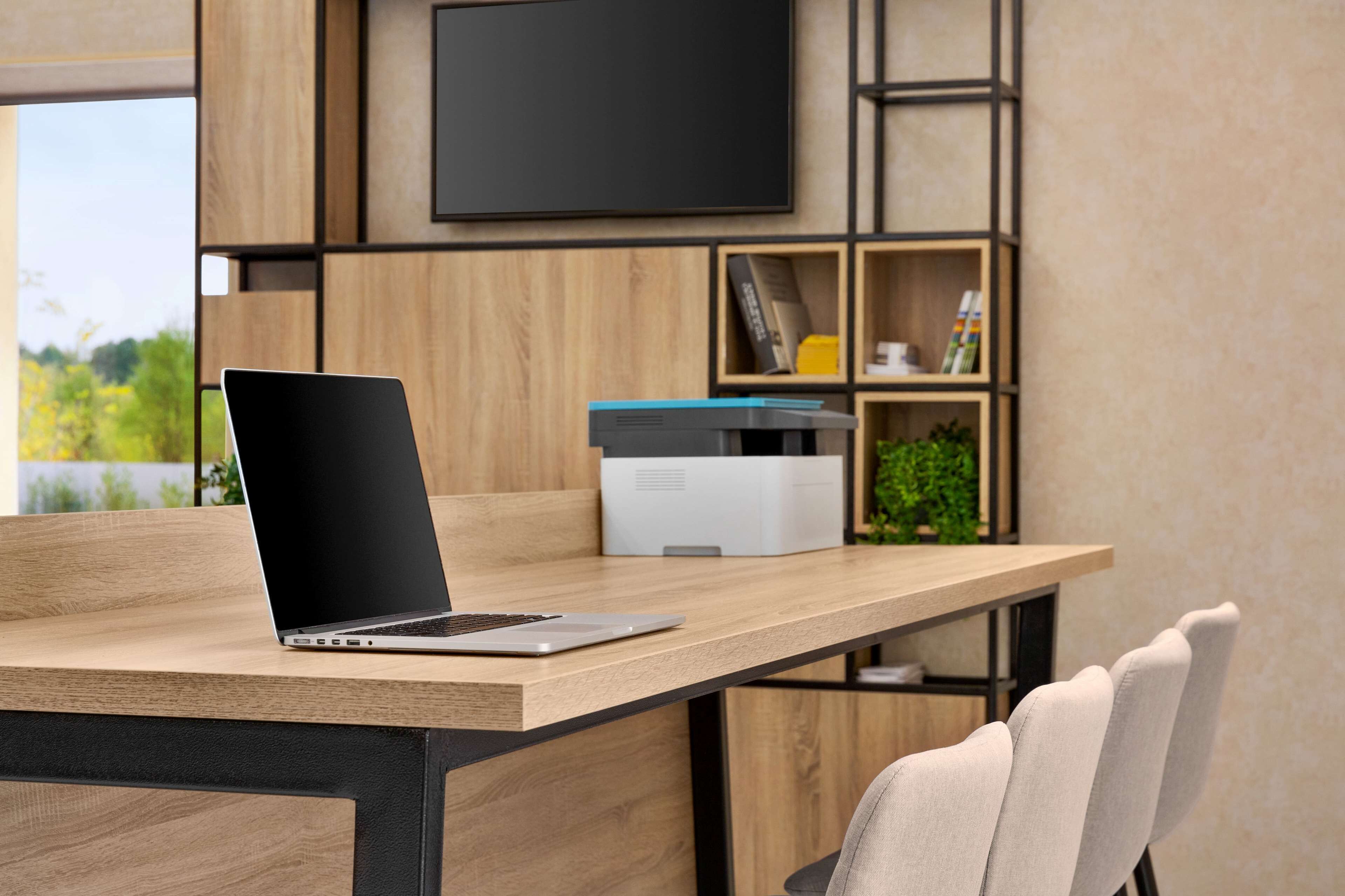 A modern office space with a wooden desk, a laptop, a printer, and a bookshelf.