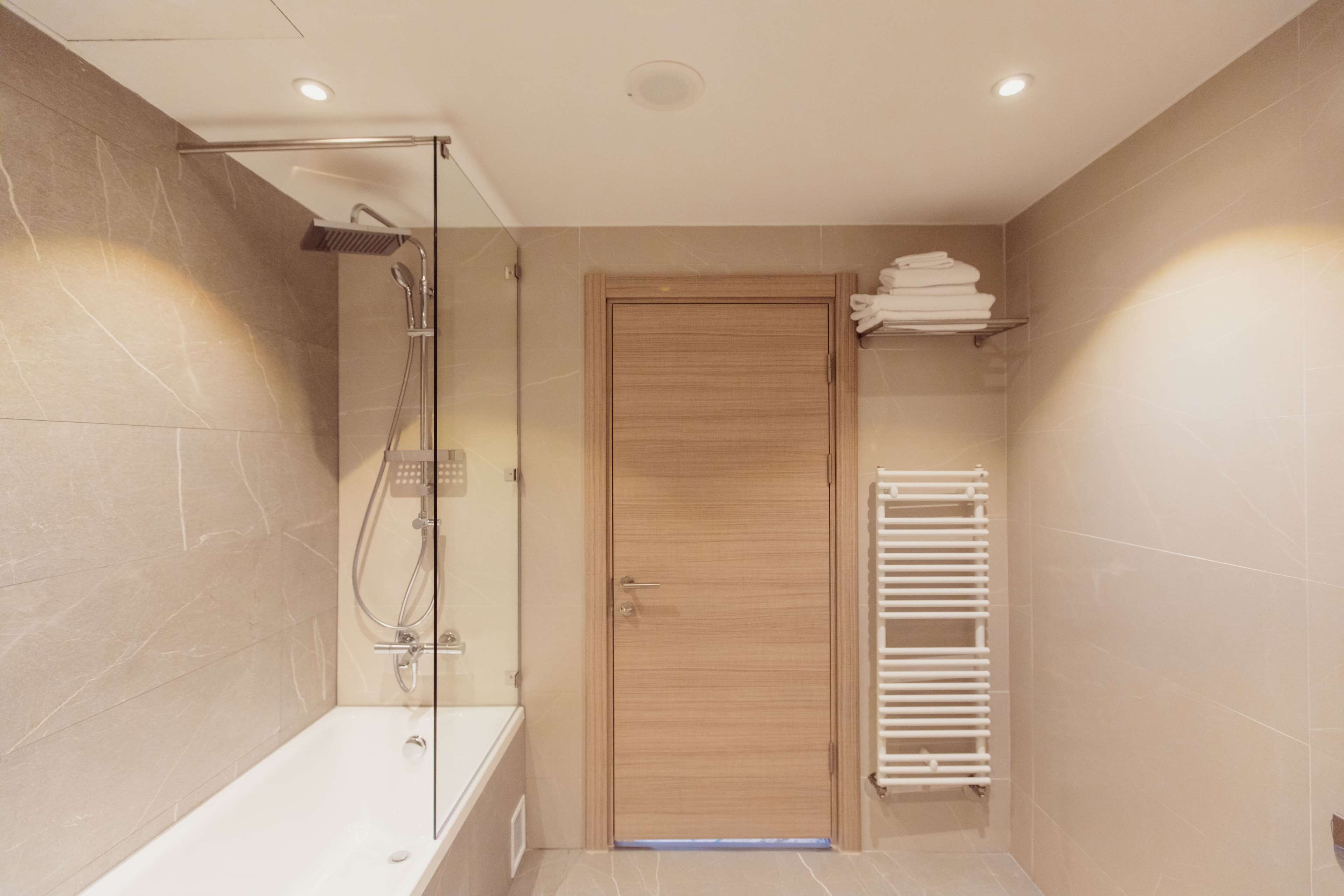 Un bagno moderno con doccia vetrata, una porta in legno e un porta asciugamani bianco.