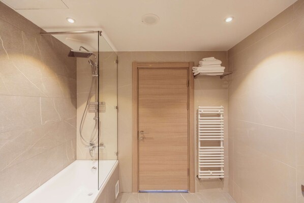 A modern bathroom with a glass-enclosed shower, a wooden door, and a white towel rack.