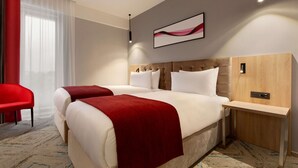 Een moderne hotelkamer met een groot bed, een nachtkastje, een rode stoel en een groot raam met transparante gordijnen.