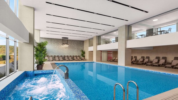 Een modern binnenzwembad met helder water, een jacuzzi-gedeelte en lounge stoelen.