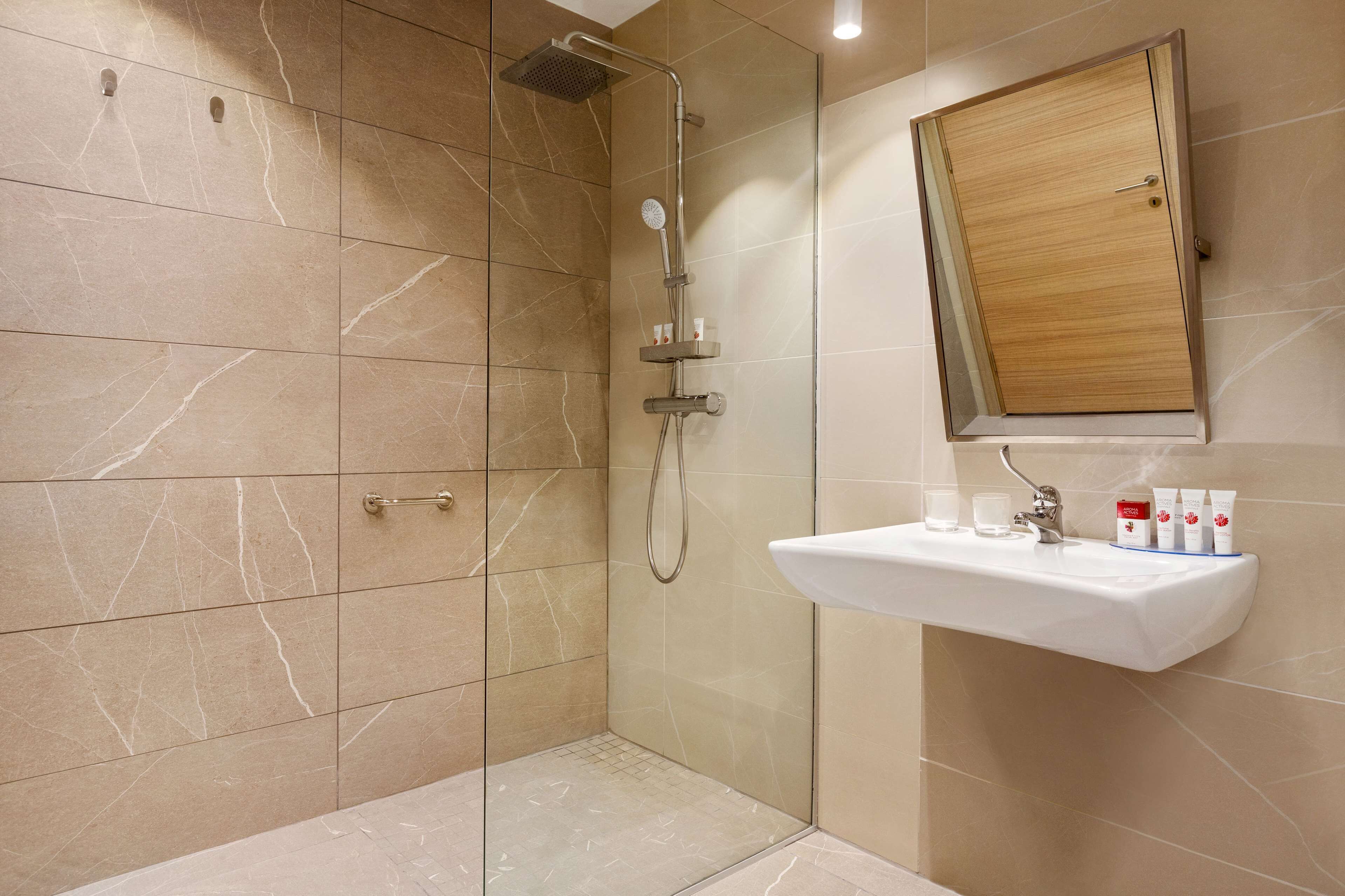 Une salle de bain moderne avec une douche à parois de verre, un meuble à pharmacie en bois et un lavabo agrémenté d’articles de toilette.