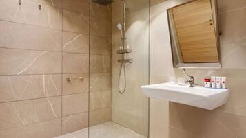 Une salle de bain moderne avec une douche à parois de verre, un meuble à pharmacie en bois et un lavabo agrémenté d’articles de toilette.