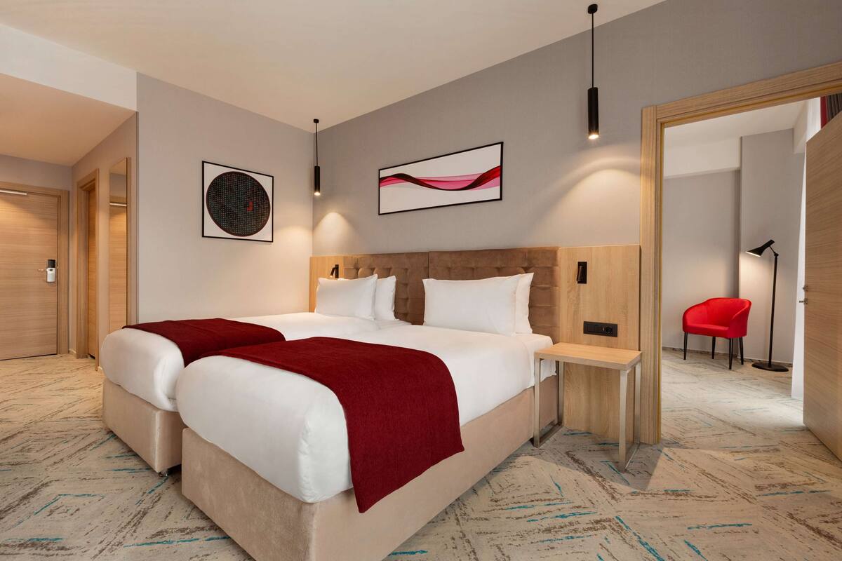 Een moderne hotelkamer met een groot bed, een houten hoofdeinde, een nachtkastje en een rode stoel.