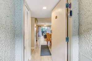 A hallway with a wooden floor, a door with a number plate, and a view into a dining area with chairs and a table.
