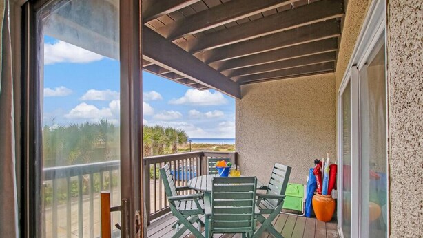 Een houten terras met een tafel, stoelen, een glazen deur en uitzicht op het strand.