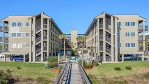 Een modern appartementencomplex met een centrale binnentuin, meerdere balkons en een houten looppad dat naar de ingang leidt.