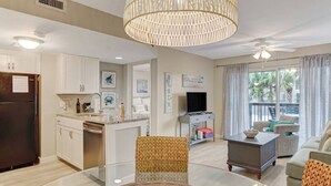Een moderne woonkamer met een glazen salontafel, een eetgedeelte met een ronde tafel, en een keuken met witte kasten.