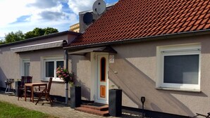 Ein Haus mit Ziegeldach, einer Haustür, einer kleinen Veranda mit Tisch und Stühlen sowie einer Satellitenschüssel.