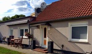 A house with a tiled roof, a front door, a small porch with a table and chairs, and a satellite dish. - Vacation apartment Paula (Senftenberg)
