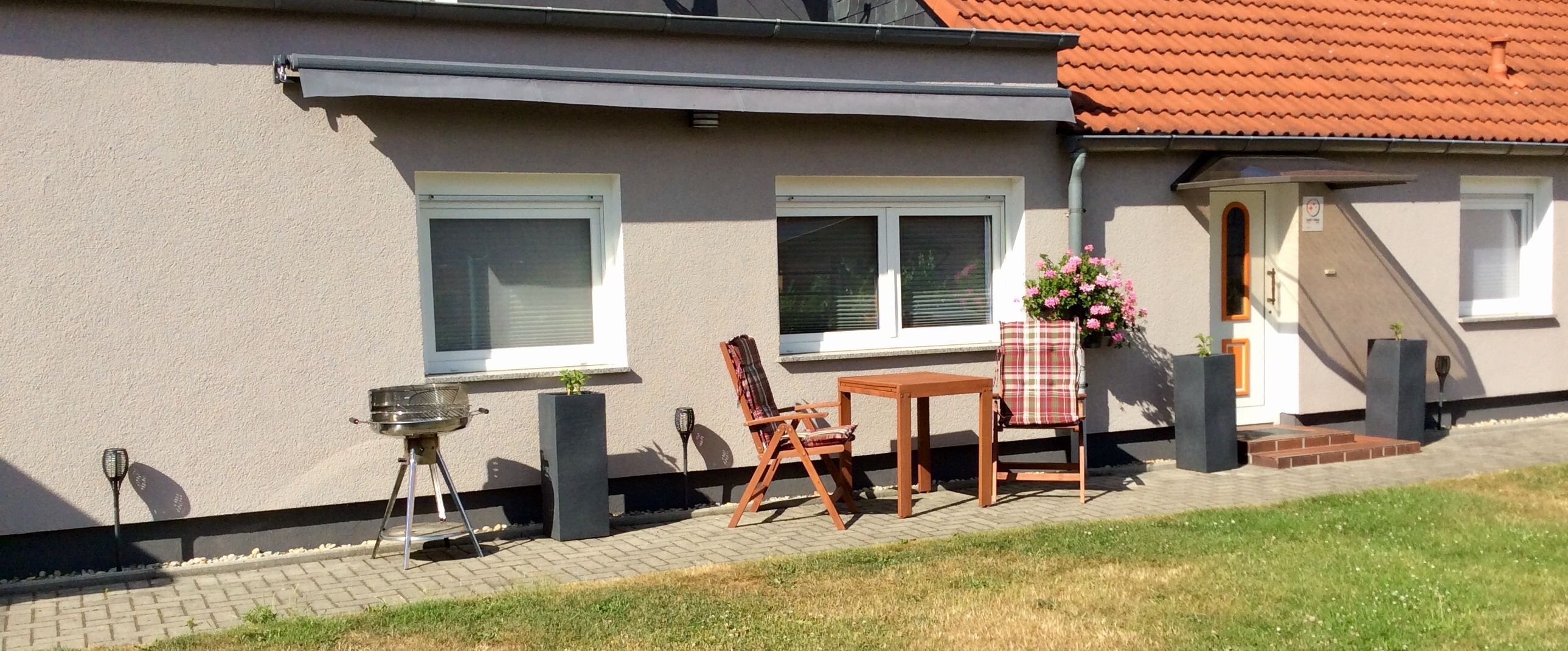 Una casa con un patio attrezzato, dotato di barbecue, tavolo e due sedie.
