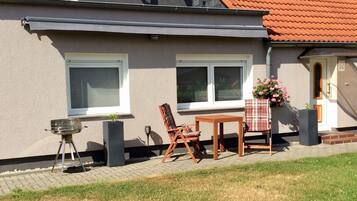 Una casa con un patio attrezzato, dotato di barbecue, tavolo e due sedie.
